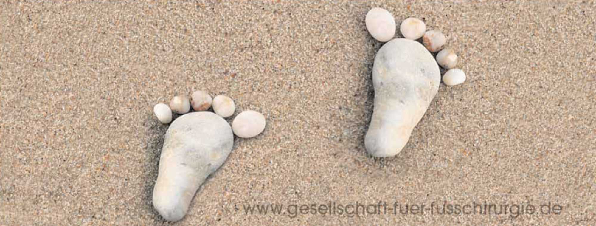Zwei mit Steinen gelegte Fußabdrücke auf Sand