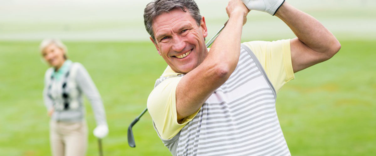 Ein Mann mit Golfschläger über der Schulter und im Hintergrund eine Golfspielerin